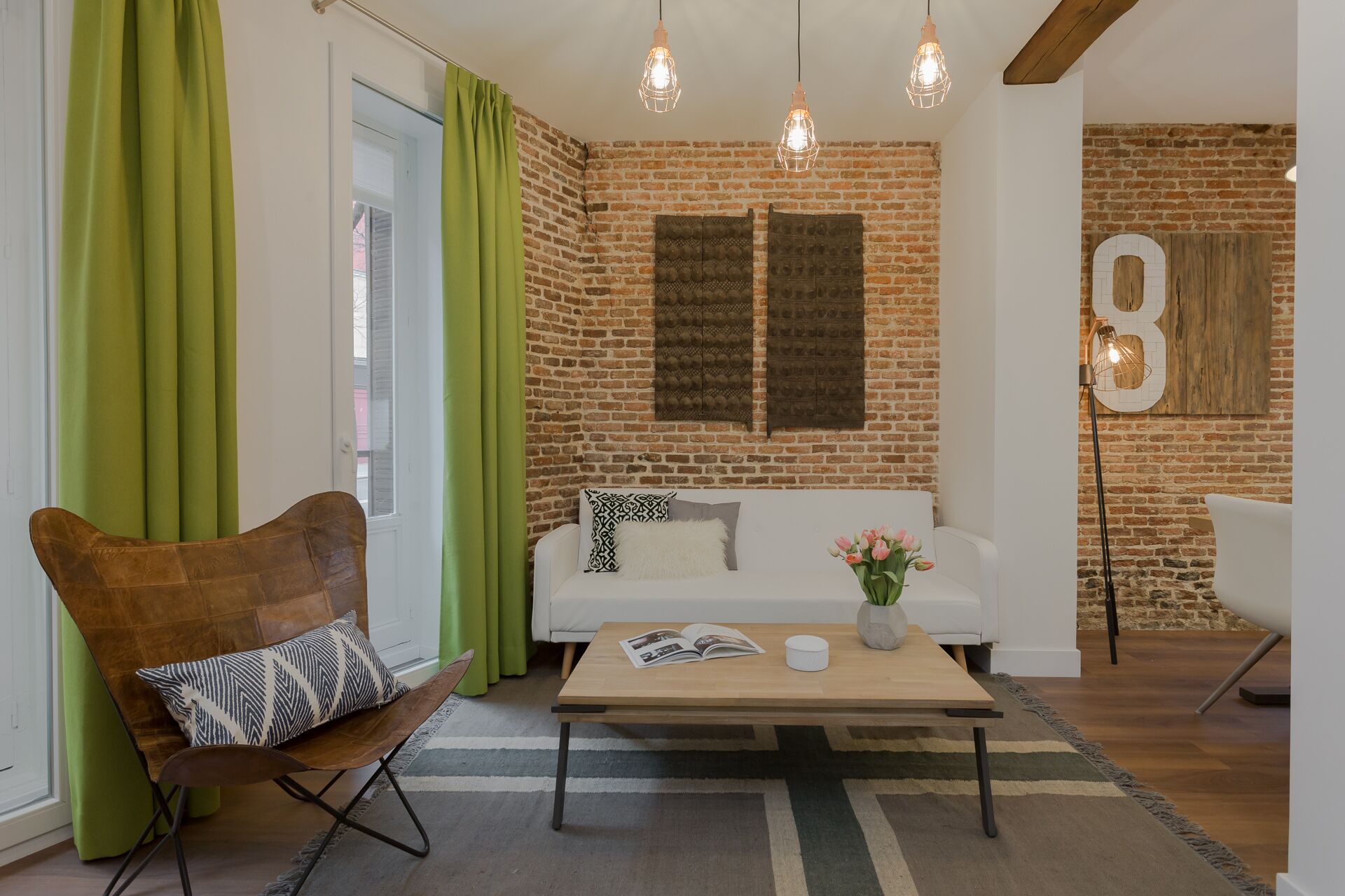 A cozy living room with a brick wall, a wooden coffee table, a white sofa, and a green chair.