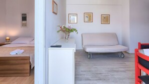 Een slaapkamer met een bed, een nachtkastje met een lamp, een kleine tafel met een bloevas, een bank en een rode stoel.