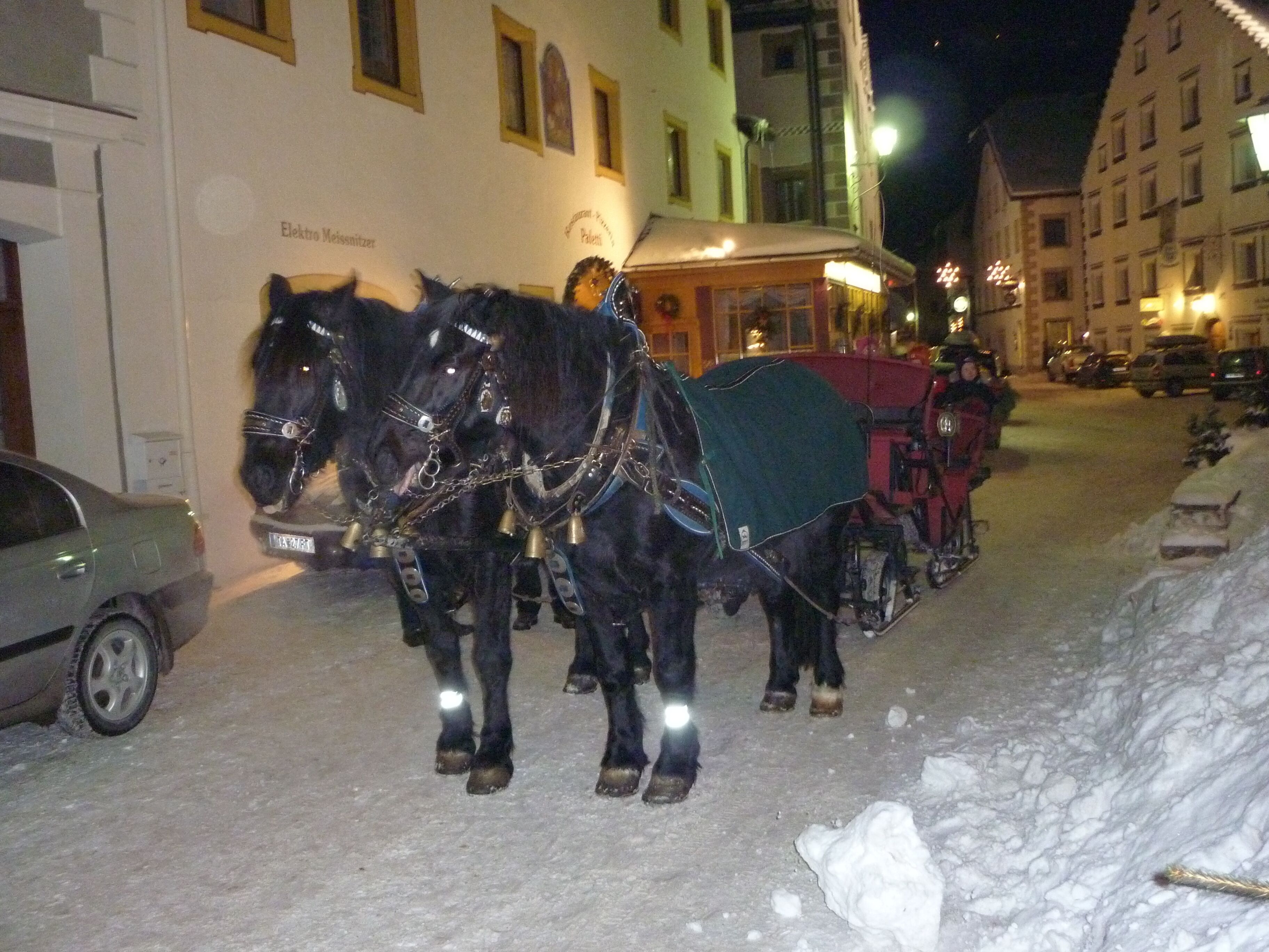 A street scene with a horse-drawn carriage and a car parked on the side of the road.