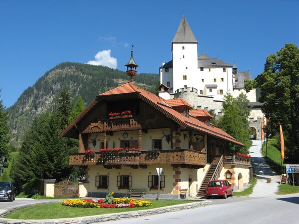 A traditional chalet with a balcony, a tower, and a mountain backdrop.