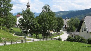 Ein ländliches Dorf mit einem markanten Kirchturm, umgeben von üppiger Vegetation und einer kurvenreichen Straße.