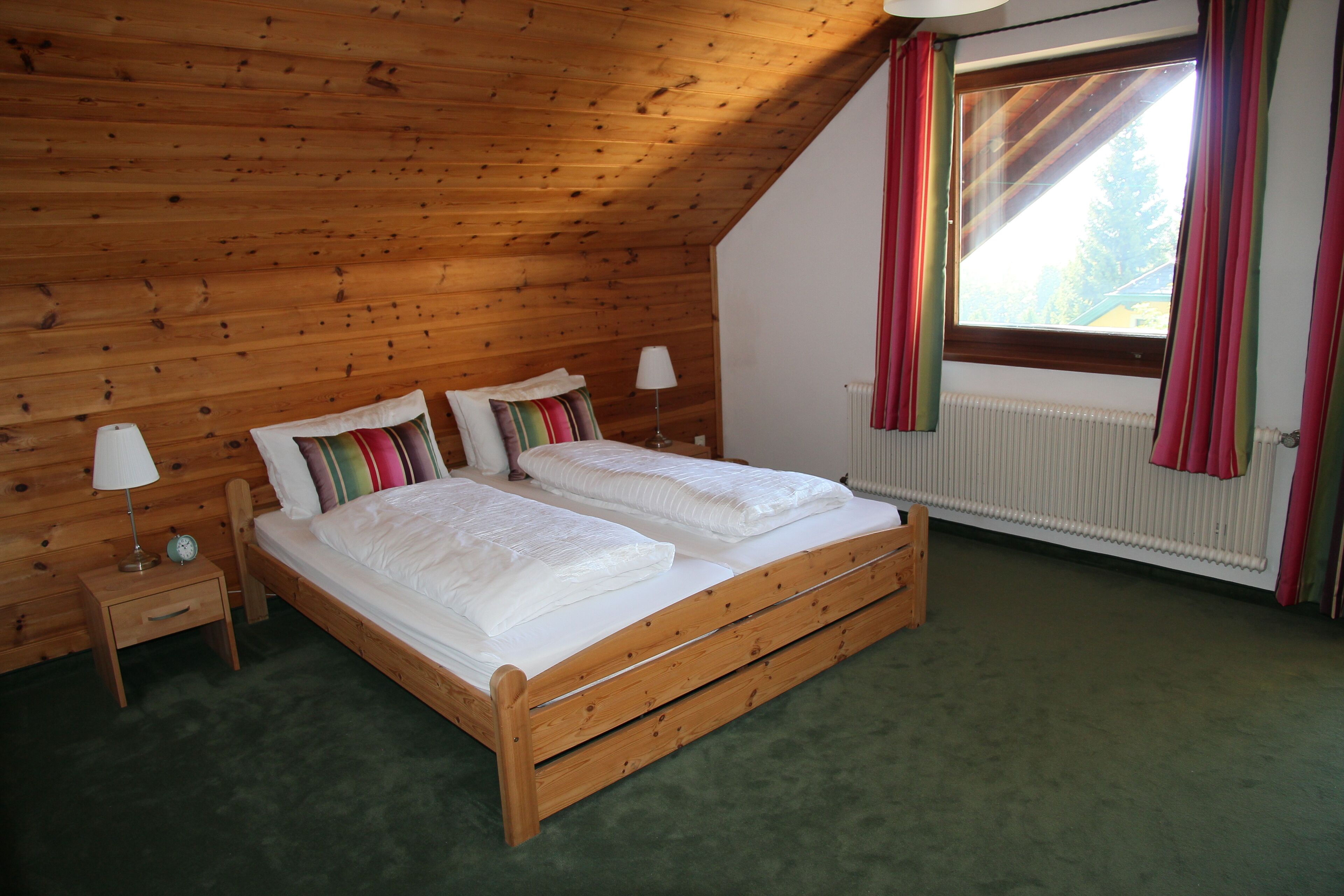 A wooden-paneled bedroom with a bed, two bedside tables, a window with curtains, and a radiator.