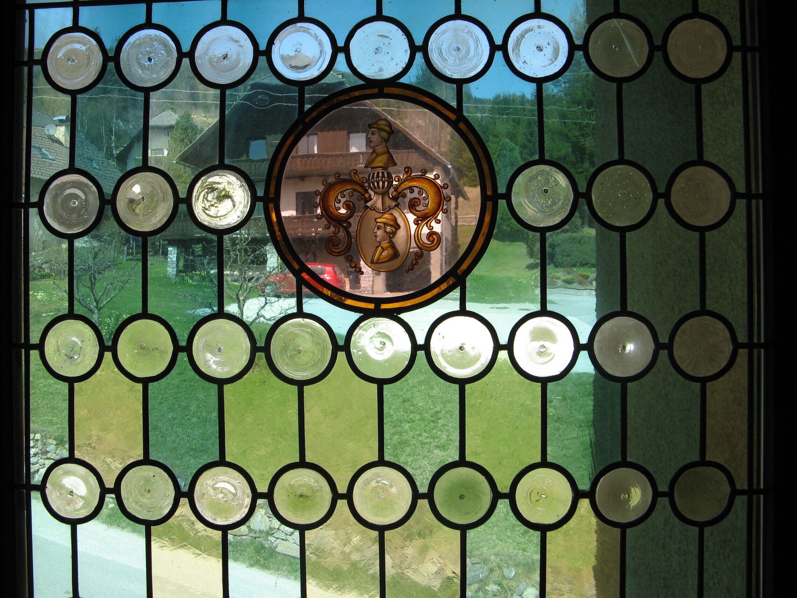 A stained glass window with a central circular design and a view of a green landscape through the window.
