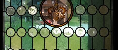 A stained glass window with a central circular design and a view of a green landscape through the window.