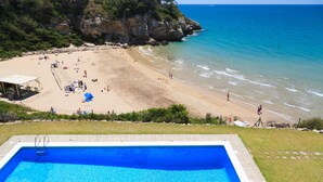 Ein Pool neben einem Strand mit klarem, blauem Wasser und einer felsigen Klippe im Hintergrund.