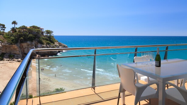 Ein Balkon mit Glasgeländer mit Blick auf einen Strand und das Meer.