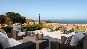 Un patio al aire libre con mobiliario de mimbre, un muro de piedra y vistas al océano.