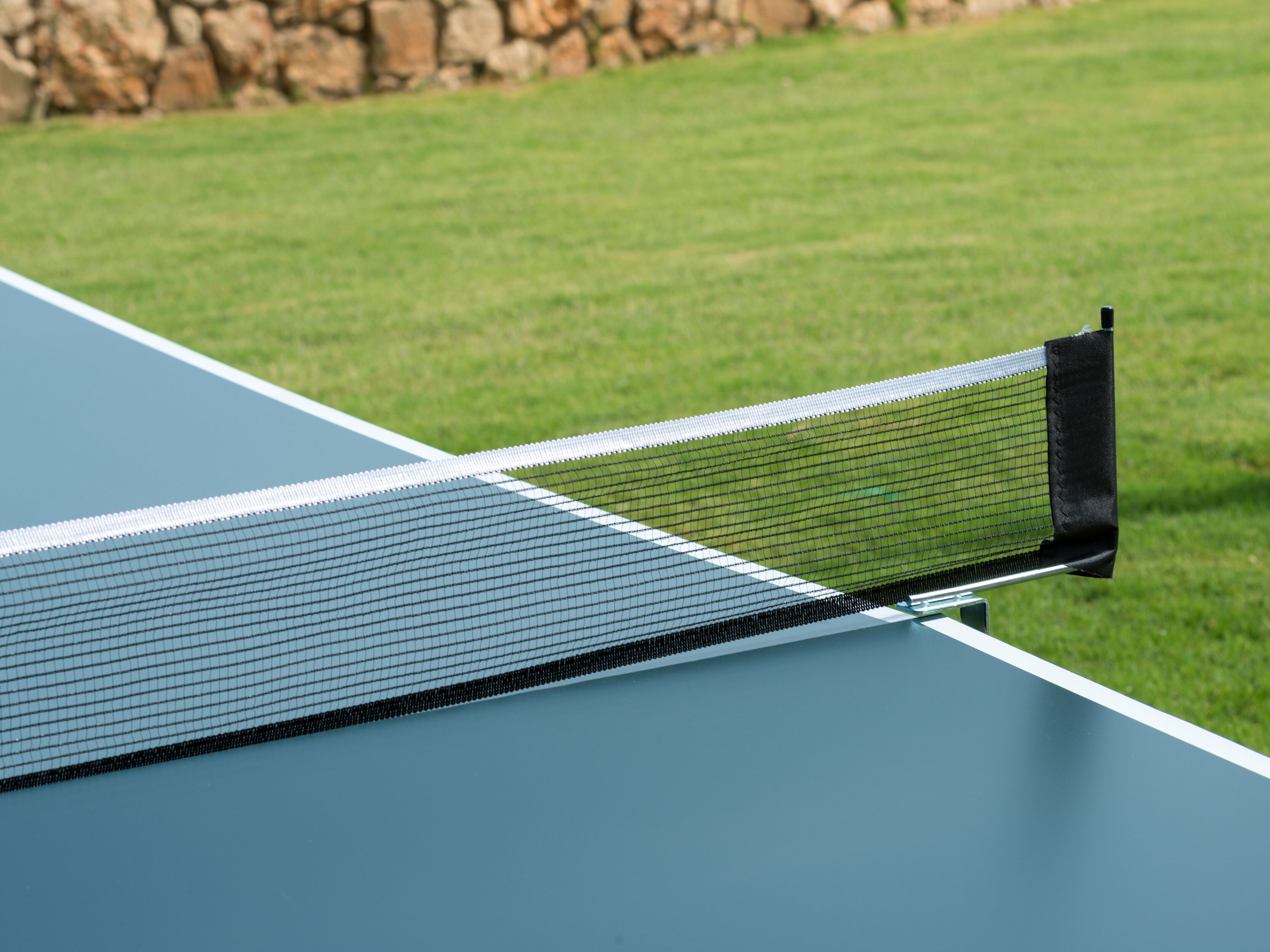 A close-up of a tennis court with a net and a stone wall in the background.