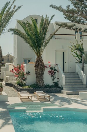 Zona de piscina con una palmera, una escalera y un edificio de fachada blanca.