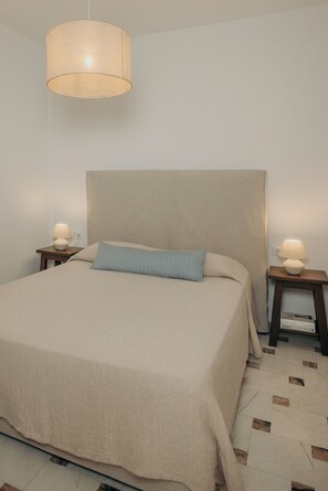 Un dormitorio con una cama grande, dos mesitas de noche, una lámpara colgante y un suelo con diseño.