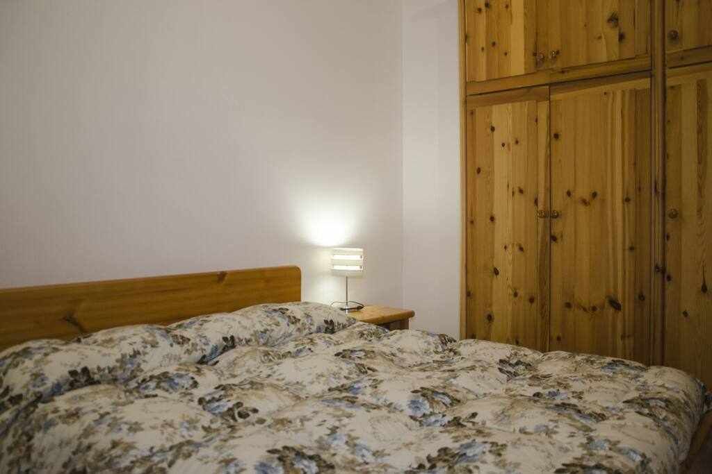 A bedroom with a wooden headboard, a floral bedspread, and a bedside lamp.