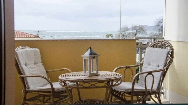 Ein Balkon mit Korbstühlen und einem kleinen Tisch, mit Blick auf ein Gewässer und eine ferne Landschaft.