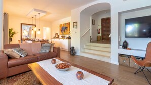 En moderne stue med sofa, sofabord og fjernsyn. En trappe fører op til et spiseområde.
