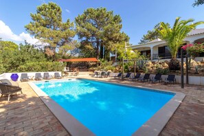A swimming pool with lounge chairs, a pergola, and a building with a white facade.