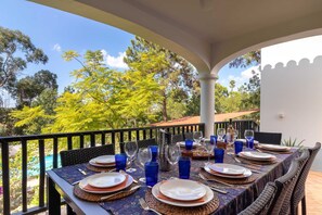 A dining table set outdoors with blue glassware, plates, and cutlery.