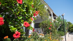A building with a white facade, a balcony with chairs, and a garden with various flowers. - Holiday home for 5 people, 200 meters from the sea and free wi-fi (Provincia di Agrigento)