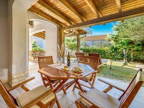 Enjoy al fresco dining in a serene garden setting, surrounded by lush greenery and a wooden pergola.