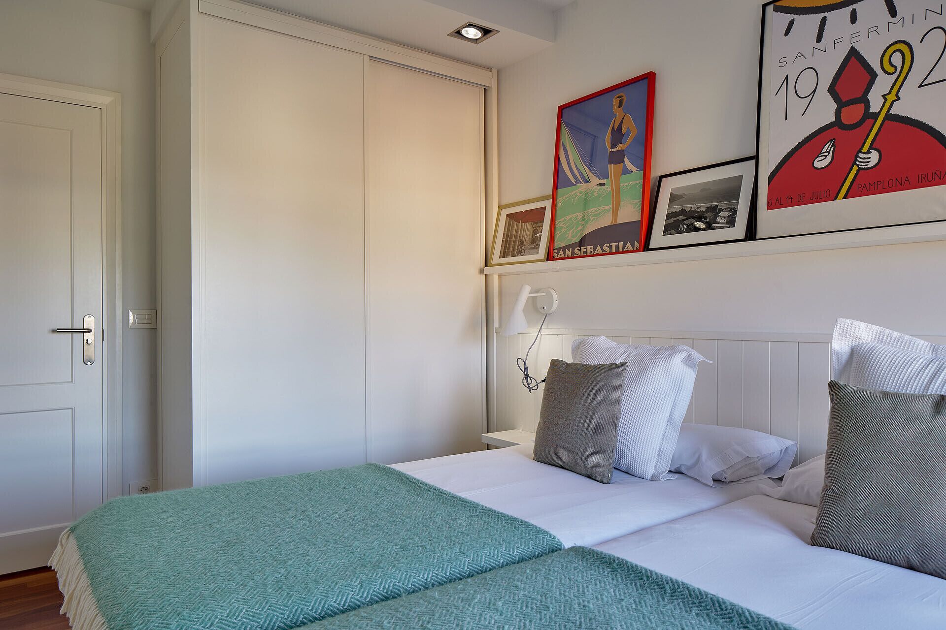 A bedroom with a bed, pillows, a nightstand, a wall-mounted lamp, and a door.