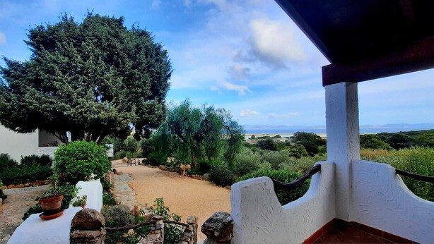 A stone pathway leading to a white building with a red roof, surrounded by greenery and a view of distant hills. - The Casetta di Merau Sant'Antioco (Sant'Antioco)