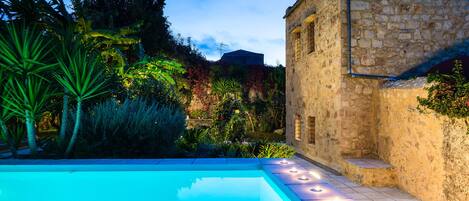Une piscine avec un bâtiment en pierre et une végétation luxuriante en arrière-plan.