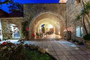 Un patio de piedra con un arco de entrada, mobiliario exterior y plantas en macetas.