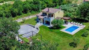 Ein zweistöckiges Haus mit Steinaußenwand, einem Pool und einer Terrasse mit Liegestühlen.