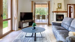 Ein Wohnzimmer mit Fernseher, Sofa, Kamin und Blick ins Freie.