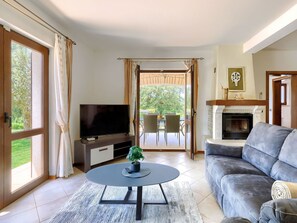 Een woonkamer met televisie, bank, open haard en uitzicht op het landschap.