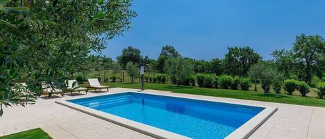 A rectangular swimming pool with a tiled deck, surrounded by a well-maintained lawn and trees.