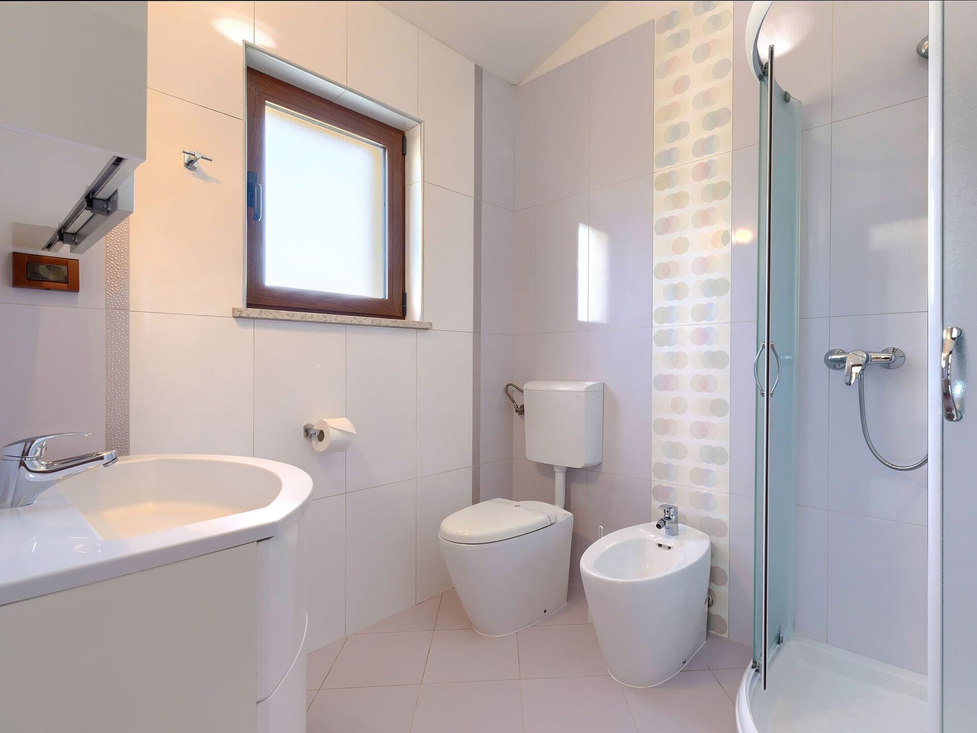 A modern bathroom with a white sink, toilet, bidet, and a glass-enclosed shower.