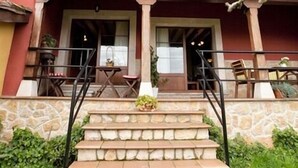 A two-story building with a stone facade, a red exterior, and a wooden balcony with chairs and a table.