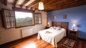 A bedroom with wooden flooring, a bed with white linens, a window with a view of hills, and a wooden ceiling.