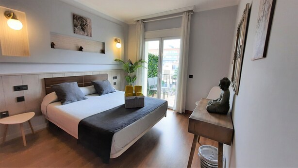 Una habitación de hotel moderna con una cama grande, un escritorio pequeño, una planta en maceta y una estatua de Buda.