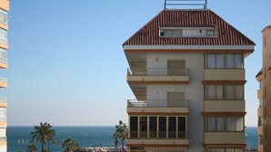 Un edificio de varios pisos con balcones, vista a la playa y palmeras.