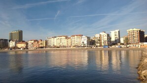 Un paisaje urbano frente al agua, con edificios de varios pisos, una masa de agua tranquila y un cielo despejado.