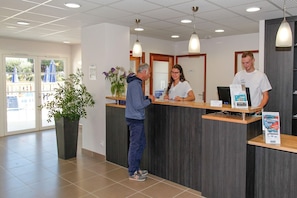A reception area with a reception desk, a potted plant, and a window with a view of the outside.