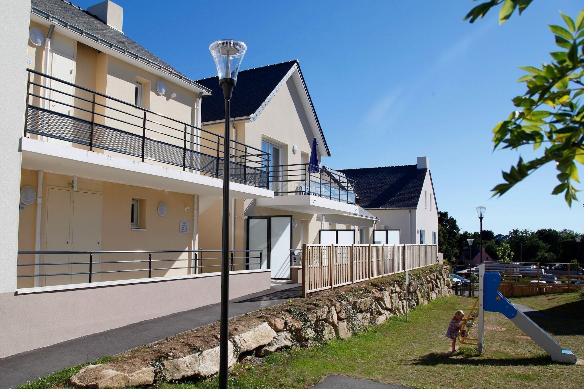A two-story building with balconies, a stone retaining wall, and a playground.