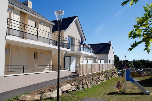 A two-story building with balconies, a stone retaining wall, and a playground.