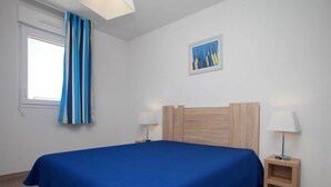 Quarto com uma cama, duas mesas de cabeceira, uma janela com cortinas, um quadro na parede e uma luminária em cada mesa de cabeceira.