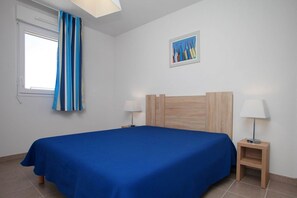 Ein Schlafzimmer mit einem Bett, zwei Nachttischen, einem Fenster mit Vorhängen, einem Bild an der Wand und einer Lampe auf jedem Nachttisch.
