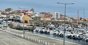 A marina with boats docked, a road with barriers, and buildings in the background.