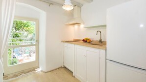 Una cocina con armarios blancos, un refrigerador blanco, una ventana con vista a follaje y un frutero sobre la encimera.