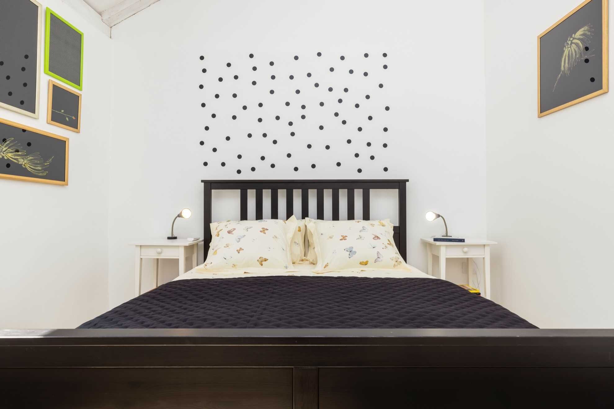 Une chambre à coucher comprenant un lit, deux tables de chevet, une lampe fixée au mur et trois tableaux encadrés.
