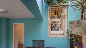 Una habitación con paredes verde azulado, una cama de madera con dos almohadas, una ventana con vista a un balcón y una pared de piedra.