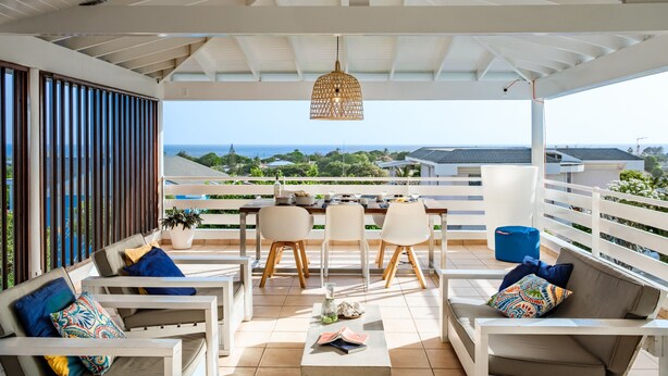 Un espace extérieur abrité, aménagé avec des meubles blancs et doté d’un luminaire suspendu, offrant une vue sur la mer.