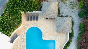 Vue aérienne d’un complexe hôtelier doté d’une grande piscine, de plusieurs espaces de détente et d’une végétation luxuriante.