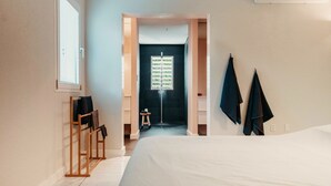 Une chambre d’hôtel avec un lit, une chaise en bois, un petit tabouret et un porte-serviettes.