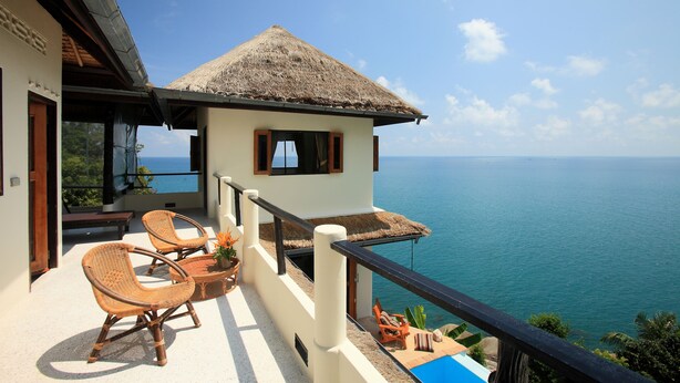 A balcony with wicker chairs, a small table, and a thatched-roof structure overlooking the sea. - White Azure (Ko Pha-ngan)