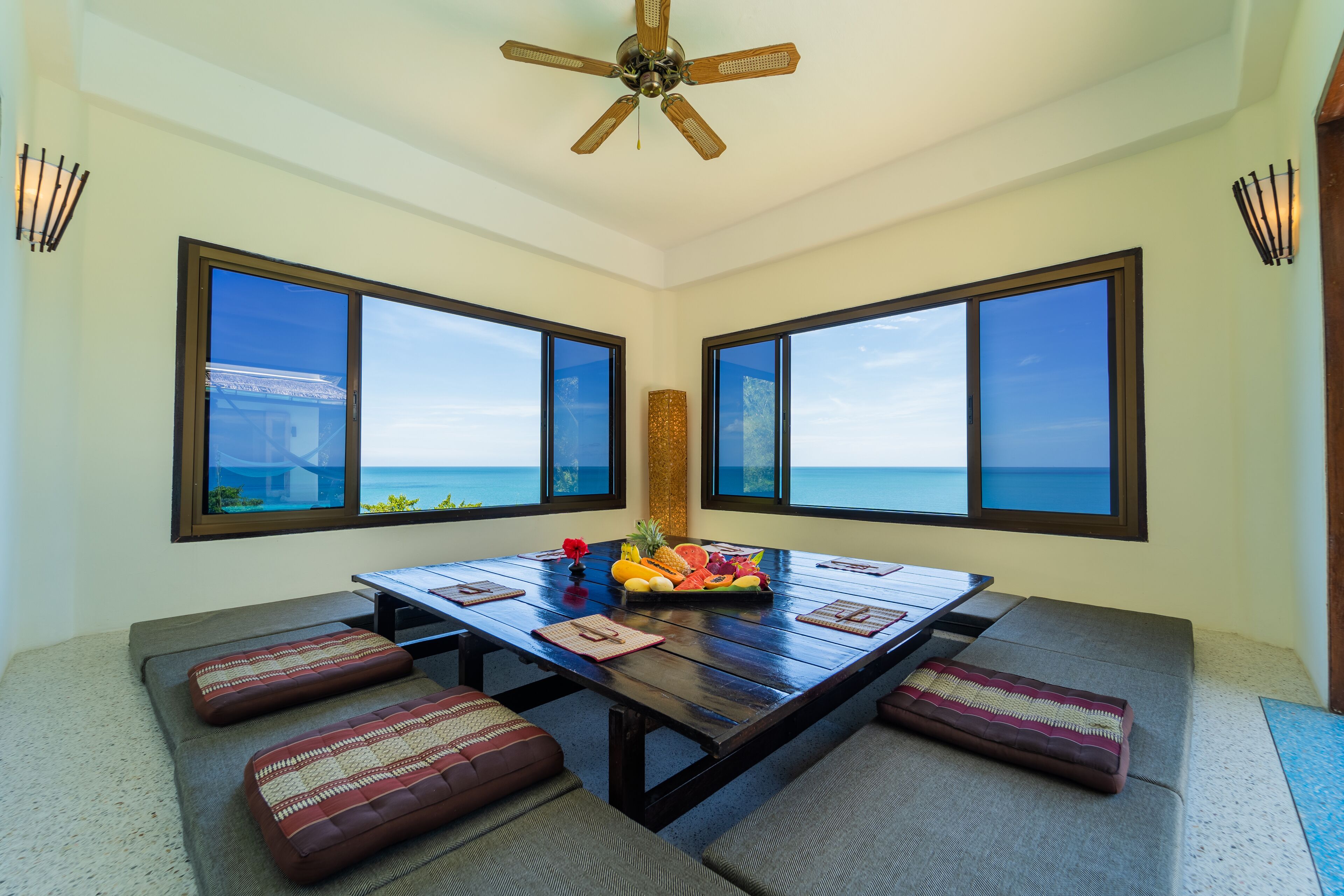 A dining area with a large table, cushioned seating, and a view of the ocean.