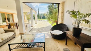 A modern living room with a glass coffee table, wicker furniture, and a view of a garden. - Entertainment-packed, Spacious, Peaceful & Convenient (Pollença)